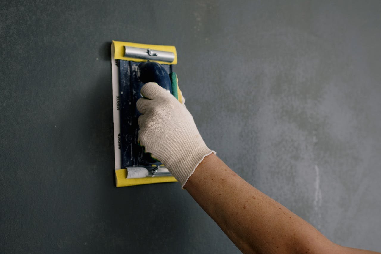 hero-img-01 Close-up of a hand smoothing a wall with a spackle tool during home renovation.