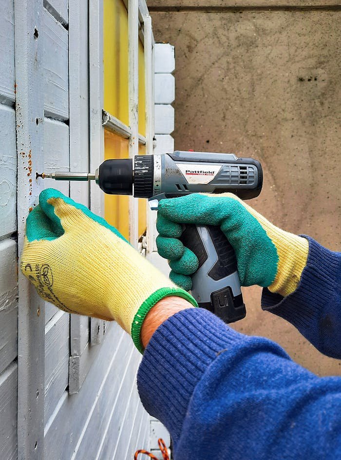 Close-up of a construction worker using a drill on a wooden wall, focusing on hands and tool.